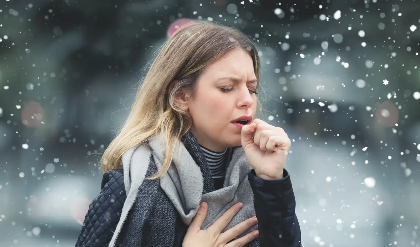 Frau hustet in ihre Hand und hält sich die schmerzende Brust aufgrund von Asthma durch Rauchen